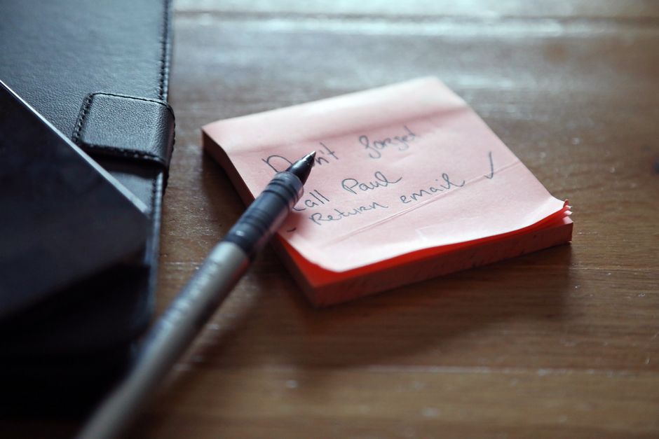 A close-up of sticky notes with a to-do list, a pen, and a wallet on a wooden desk.